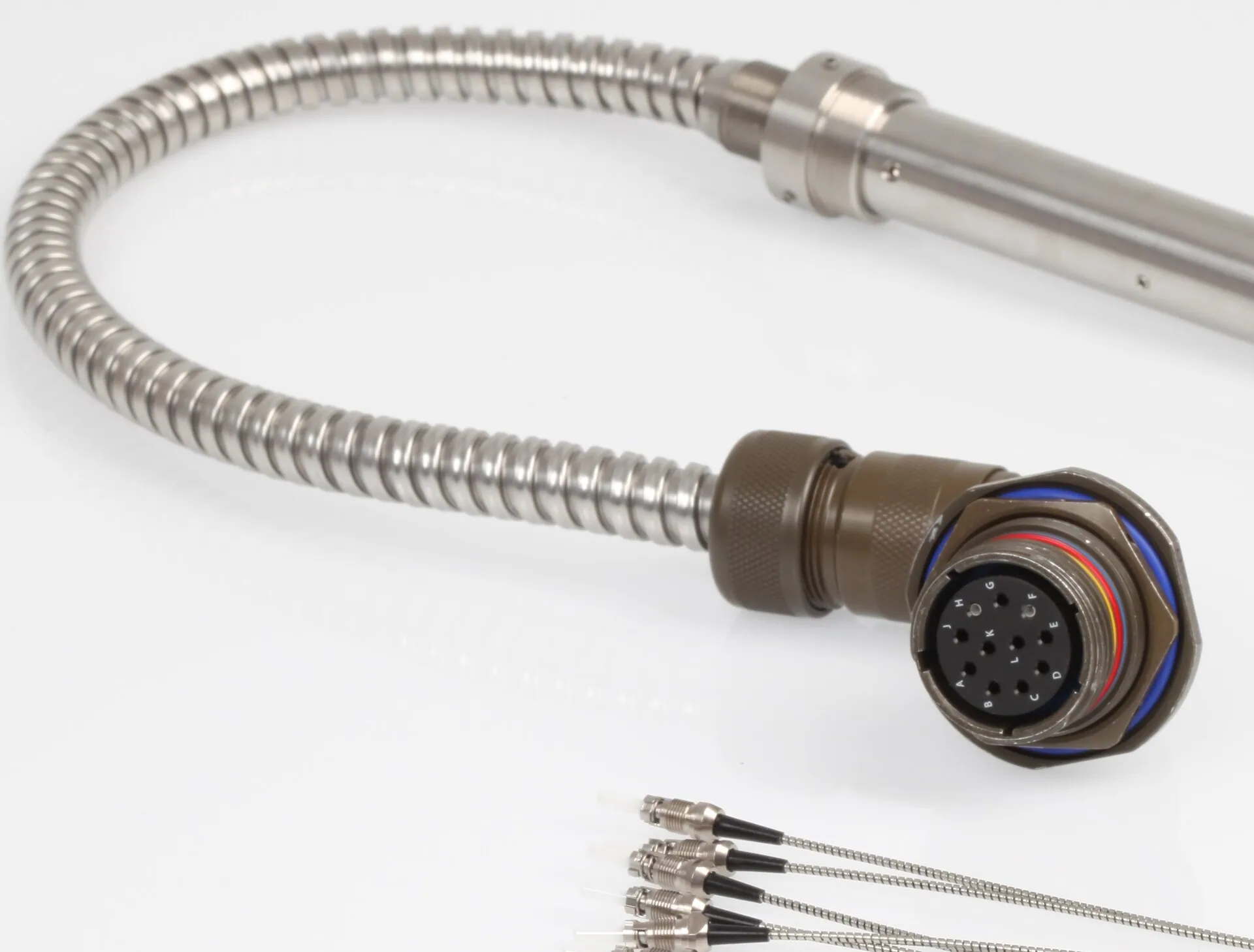 A detailed product shot of a flexible, braided metal cable terminating in a large, multi-pin military-grade circular connector.