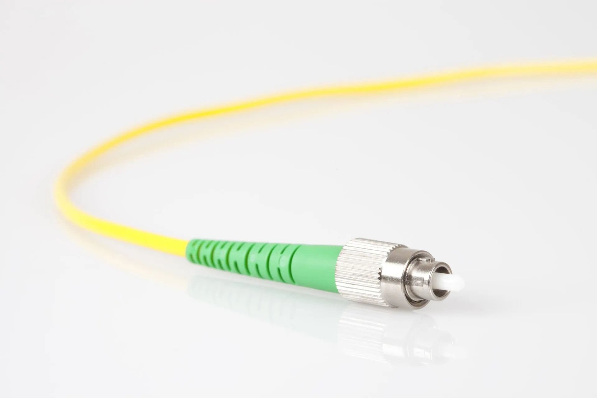 A close-up of a yellow fibre optic cable that terminates in a silver connector with a green, textured plastic housing, likely a single-mode SC/APC type.