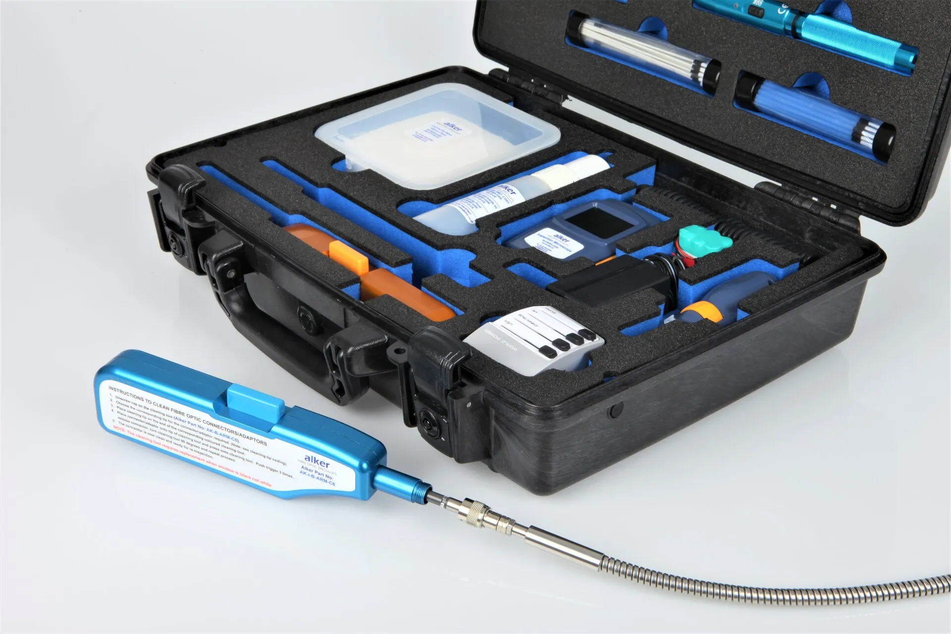 An open, black hard-shell tool case with a custom-cut blue foam interior holds various fibre optic tools and cleaning supplies. In the foreground, a blue-handled cleaning tool with the Alker logo is connected to a braided metal cable.